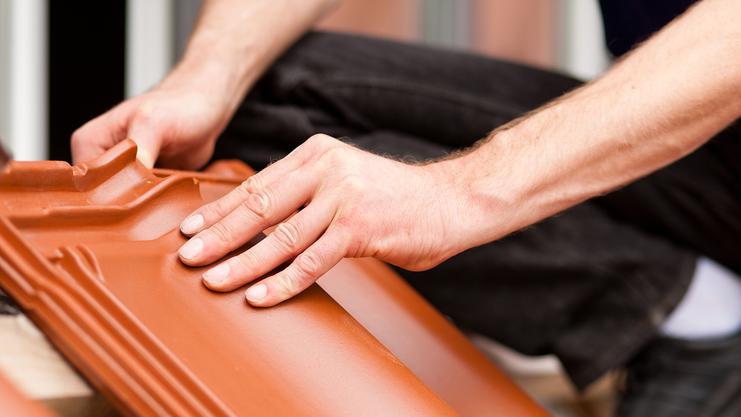 Arbeiter verlegt Dachziegel auf einer Baustelle, Hände drücken einen Ziegel an seinen Platz.