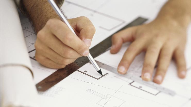 Nahaufnahme einer Hand, die mit einem Bleistift einen Plan auf Transparentpapier zeichnet, mit einem Lineal zur Unterstützung.