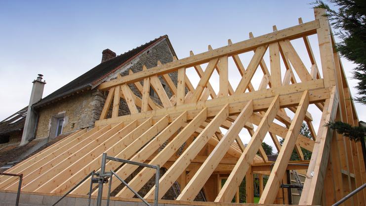 Holzgerüst eines Daches im Bau über einem alten steinernen Gebäude, mit einer Treppe und Holzlatten sichtbar.