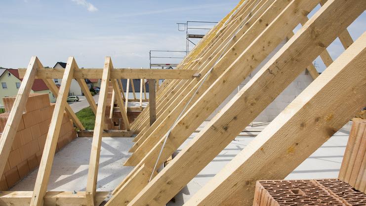Blick auf eine Dachkonstruktion mit Holzsparren und Ziegelsteinen auf einer Baustelle unter blauem Himmel.